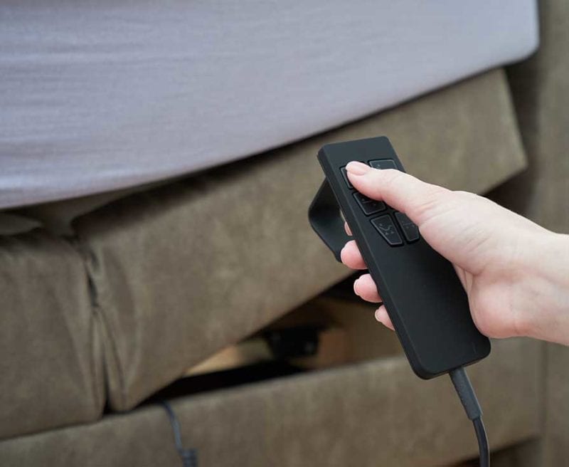 Female hand and remote control to adjust the tilt of the bed mattress, close-up